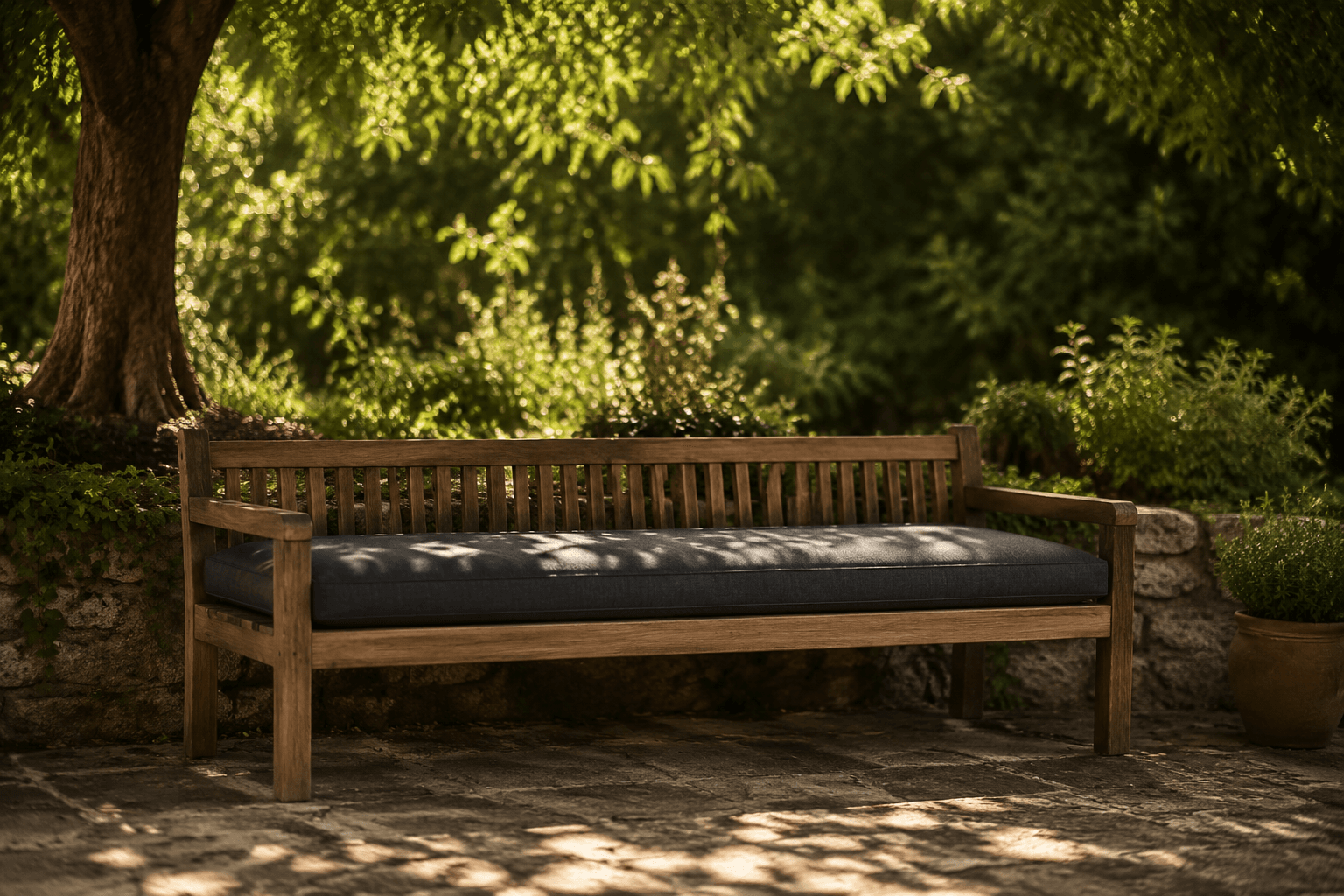 A garden bench with a long cushion under dappled afternoon light